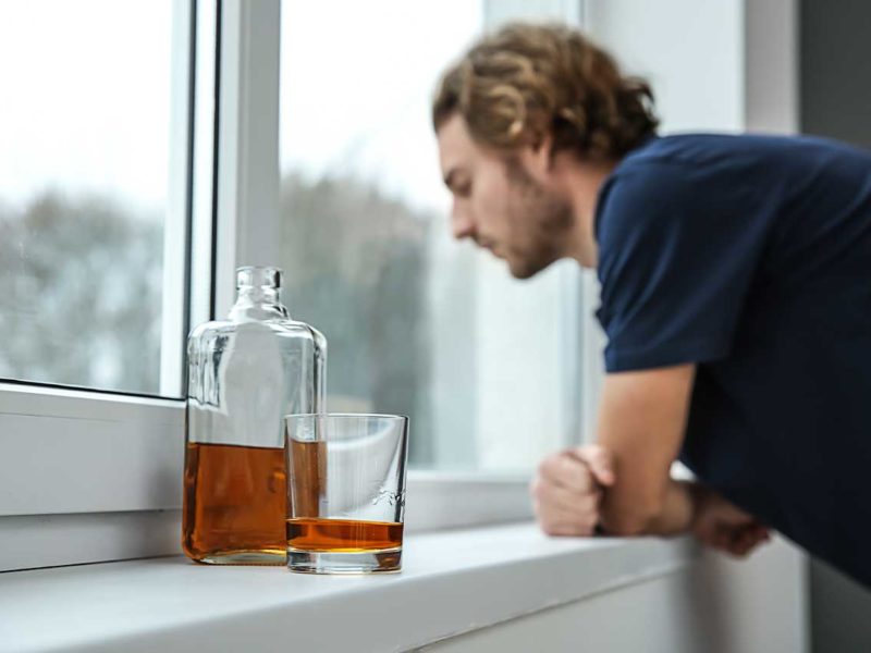 man looking out of his window with alcohol in the foreground