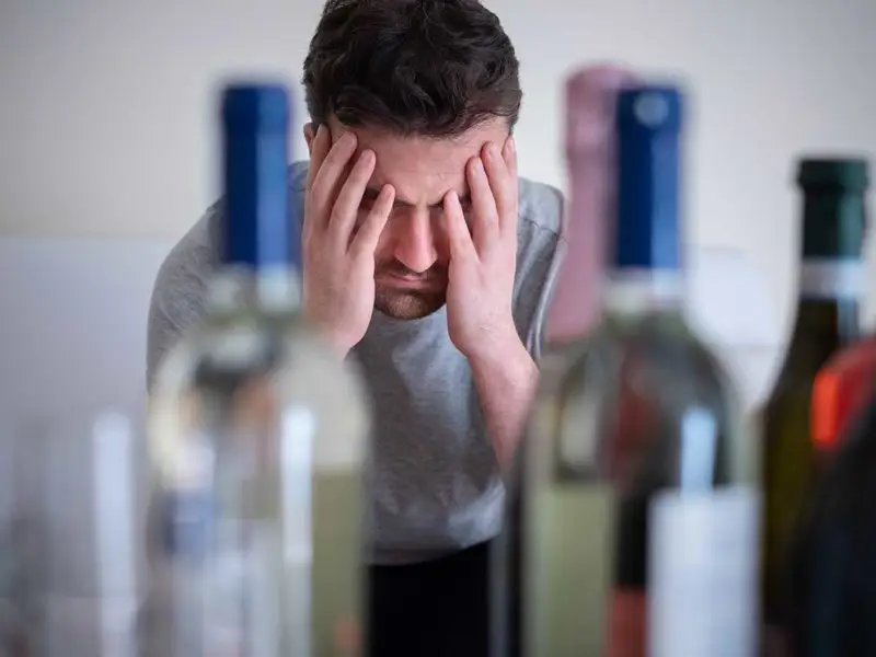 man sitting in front of bottles of alcohol with his hands over his face