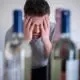 man sitting in front of bottles of alcohol with his hands over his face