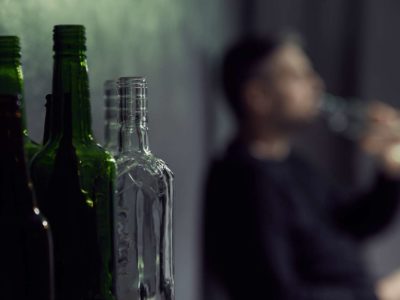 man drinking alcohol with bottles of alcohol in the frame