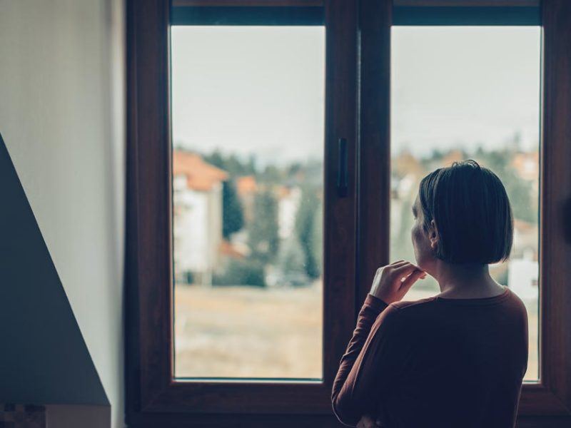 woman standing in front of her window looking outside