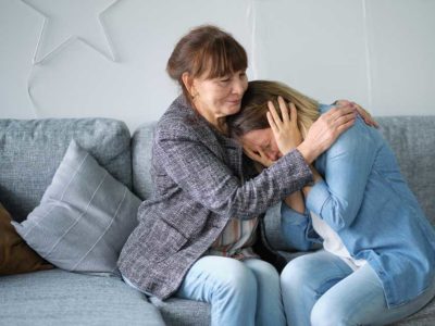 mom comforts addicted daughter while sitting on their couch