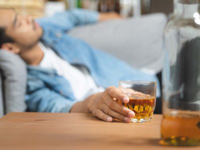 man with insomnia lying on a couch with an alcoholic drink in his hand