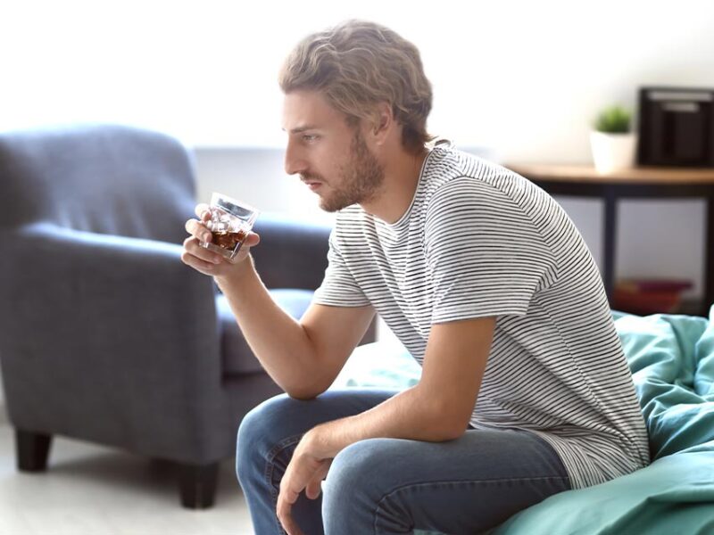 man sitting on a couch with a glass of dark liquor