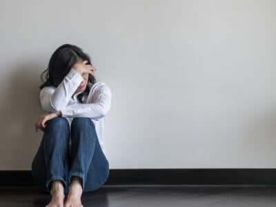 woman displaying signs of anxiety and stress while sitting against a wall.