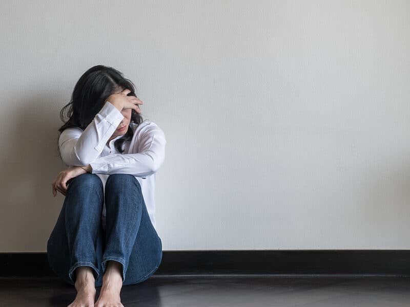 woman displaying signs of anxiety and stress while sitting against a wall.