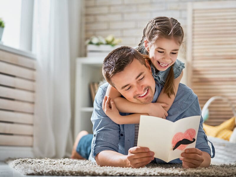 father with card and daughter on carpet