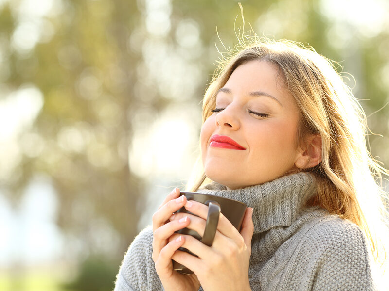 lady smiling and clutching coffe mug with eyes shut