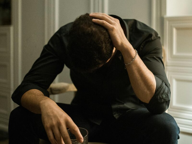 Man with glass holding his head