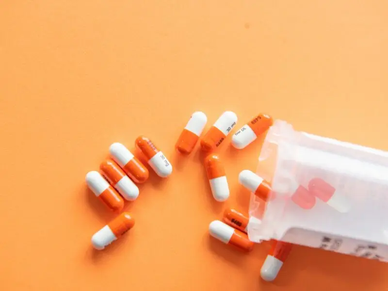 Orange and white capsule pills spilling from prescription bottle