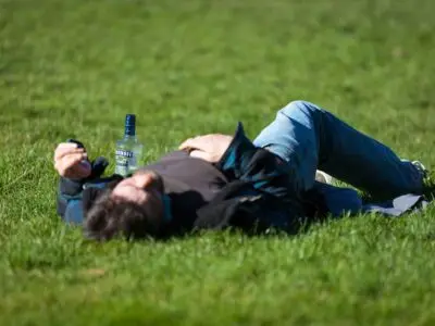 A man is laying in a field, blacked out from alcohol