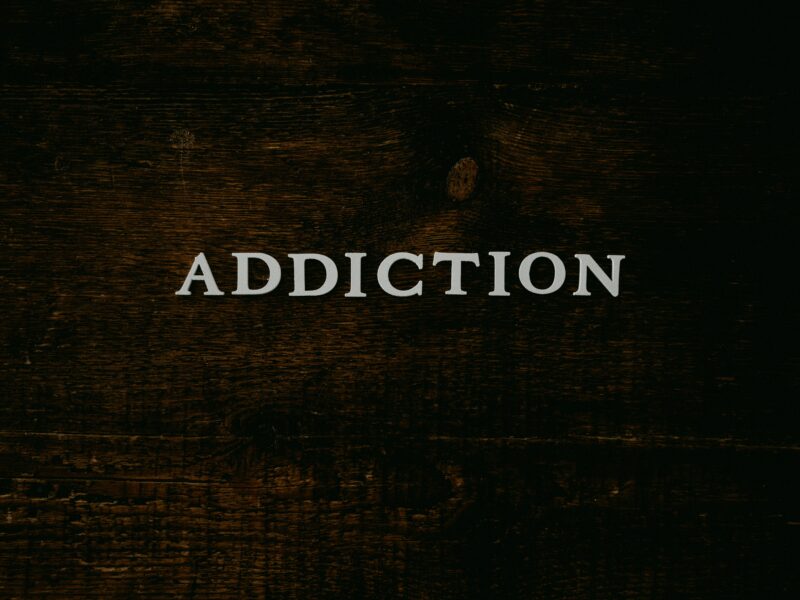 the word addiction on a dark wood background