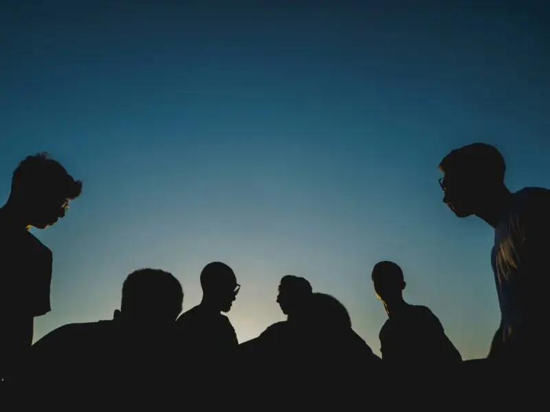 a group of individuals shrouded in darkness, symbolizing the dangers of peer pressure