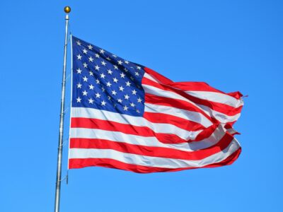 the American Flag on a pole flowing against a bright blue sky.