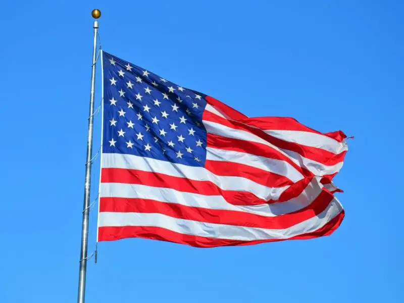 the American Flag on a pole flowing against a bright blue sky.