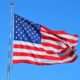 the American Flag on a pole flowing against a bright blue sky.