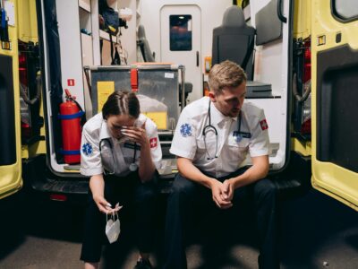 two first responders sitting in the back of their rig hunched over