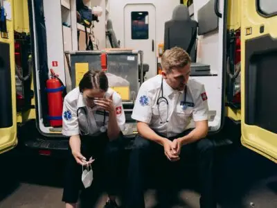 two first responders sitting in the back of their rig hunched over