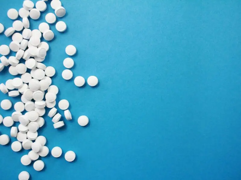 Scattered white pills on a blue background, representing prescription drug dependence and medical detox treatment.