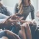 Group therapy session with people seated in a circle, one person gesturing while speaking during discussion.