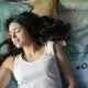 Woman resting peacefully on a bed with soft pillows, smiling with eyes closed.