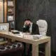 Stressed businessman in a suit sits at an office desk with his hand on his forehead, surrounded by papers and coffee.