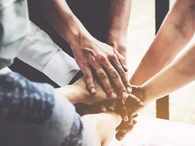 Group of people joining hands together in unity, symbolizing support and recovery community.