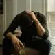 Man sitting with head in hand holding a glass of alcohol, struggling with addiction.