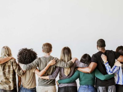 Diverse group of people standing with arms around each other, showing support and community in recovery.
