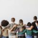 Diverse group of people standing with arms around each other, showing support and community in recovery.