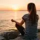 Woman meditating peacefully on rocks by the water at sunset along the Mississippi Gulf Coast.