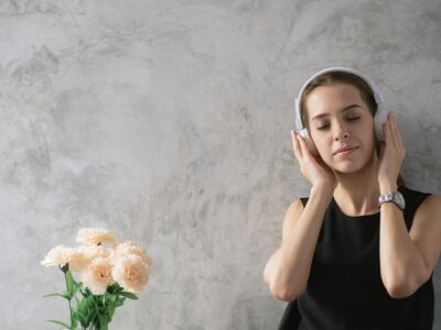 Woman with eyes closed listening to headphones peacefully beside a bouquet of flowers.