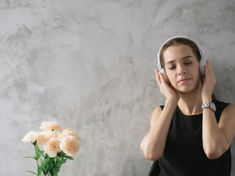 Woman with eyes closed listening to music through headphones beside a bouquet of flowers, relaxing peacefully.