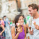 Smiling couple enjoying ice cream cones together outdoors in a busy city plaza.