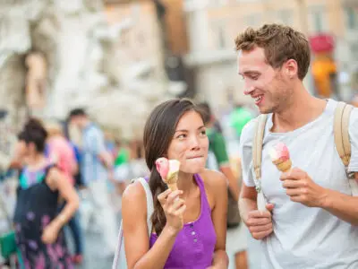 Smiling couple enjoying ice cream cones together outdoors in a busy city square.
