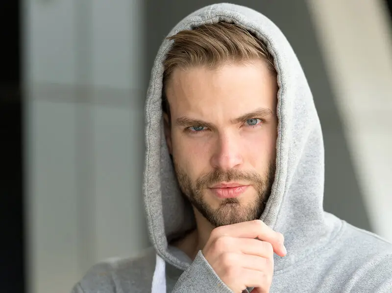 Young man in a gray hoodie with a serious, thoughtful expression looking directly at the camera.