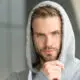 Young man in a gray hoodie with a serious, thoughtful expression looking directly at the camera.