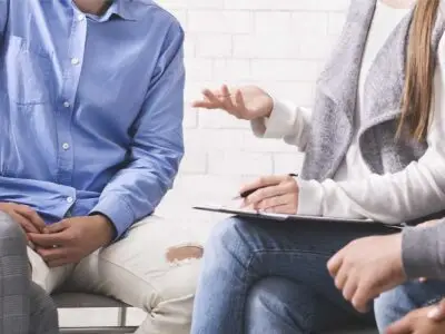 Counselor with clipboard leading a group therapy session with participants seated together during addiction treatment.