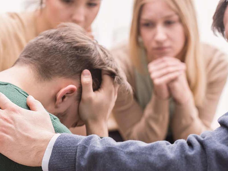Group therapy session with peers comforting an emotional man during addiction recovery support.