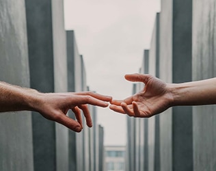 Two hands reaching toward each other between tall stone pillars, symbolizing support and connection in recovery.