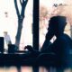 Silhouette of a person talking on the phone beside a laptop and coffee cup near a sunlit window.