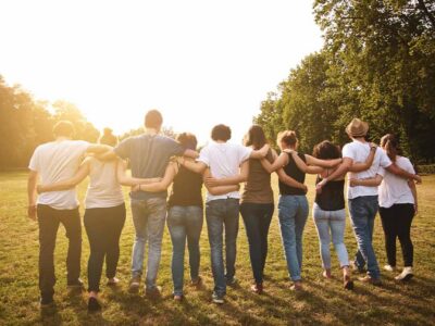 Group of people standing arm in arm in a sunlit park, symbolizing support and community in addiction recovery.
