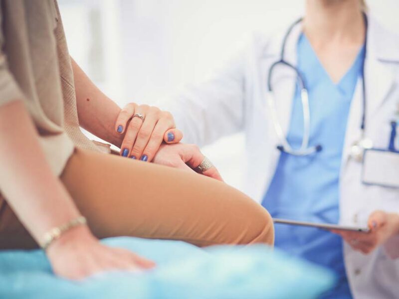 Compassionate doctor placing a reassuring hand on a patient during a supportive medical consultation.
